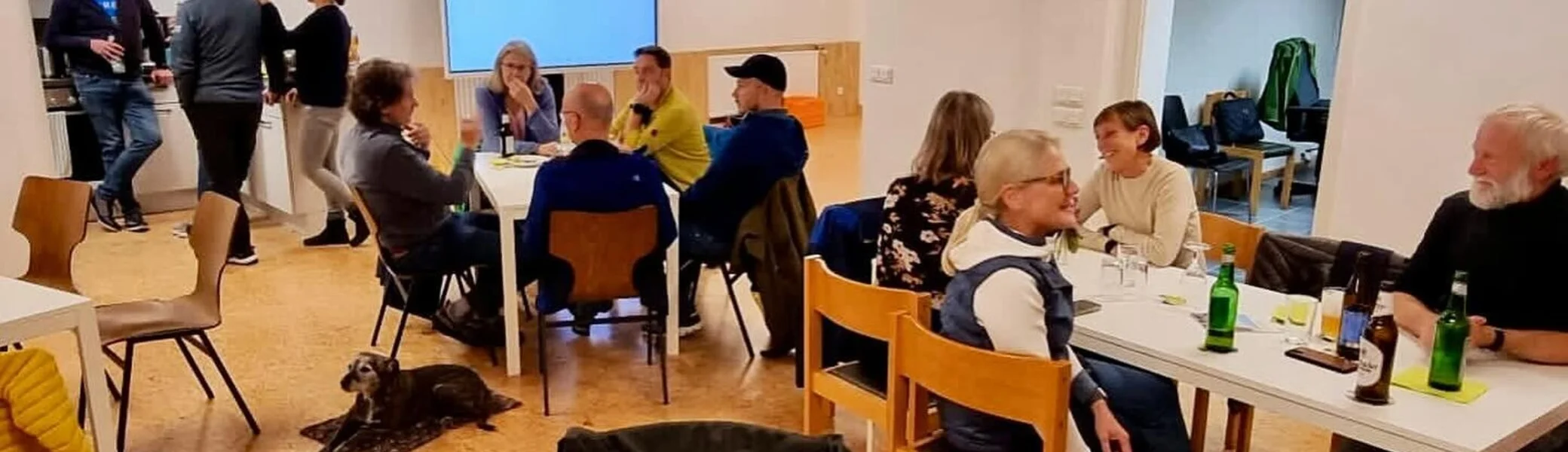 Mehrere Personen sitzen an Tischen in einem hellen Raum, unterhalten sich und trinken. | © DAV Dortmund