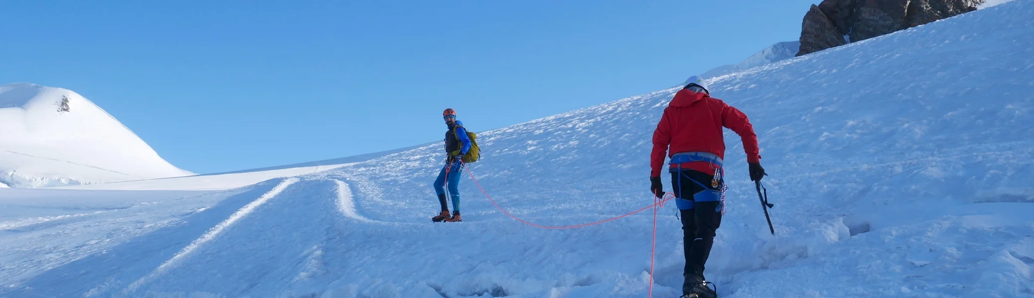 Zwei Alpinist*innen in Seilschaft überqueren einen verschneiten Gletscher bei strahlend blauem Himmel. | © DAV Dortmund