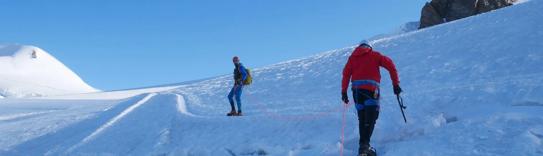 Zwei Alpinist*innen in Seilschaft überqueren einen verschneiten Gletscher bei strahlend blauem Himmel. | © DAV Dortmund