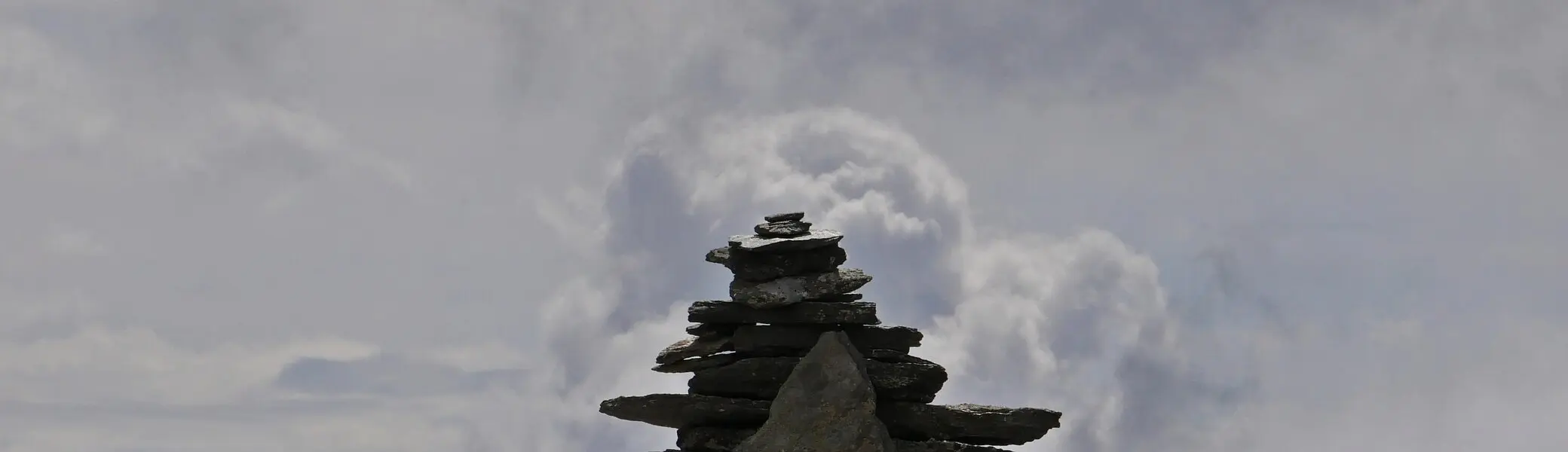 Ein sorgfältig gestapeltes Steinmännchen vor dramatischer Wolkenkulisse auf einem Gipfel. | © DAV Dortmund