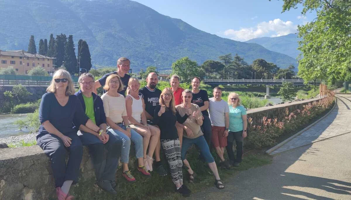 Gruppe von DAV-Mitgliedern sitzt lachend auf einer Mauer an einem Fluss mit Bergen im Hintergrund. | © DAV Dortmund