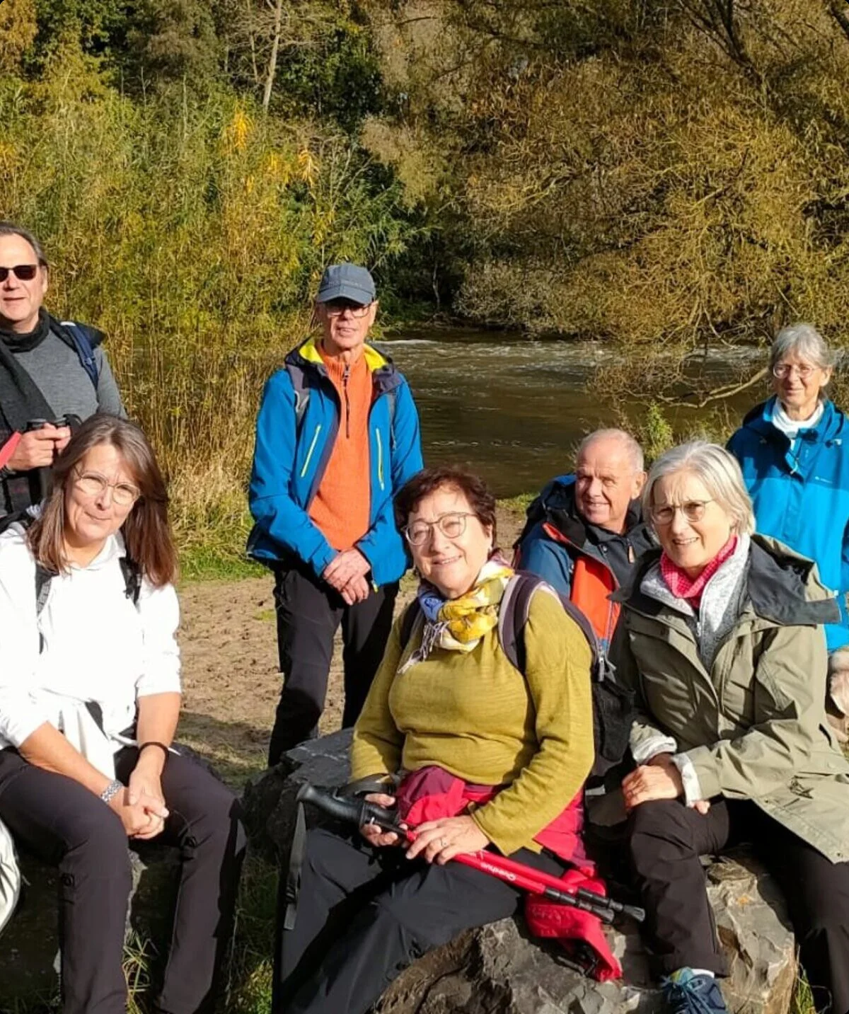 Gruppe von Wander*innen sitzt und steht entspannt auf Steinen an einem Flussufer bei sonnigem Wetter. | © DAV Dortmund