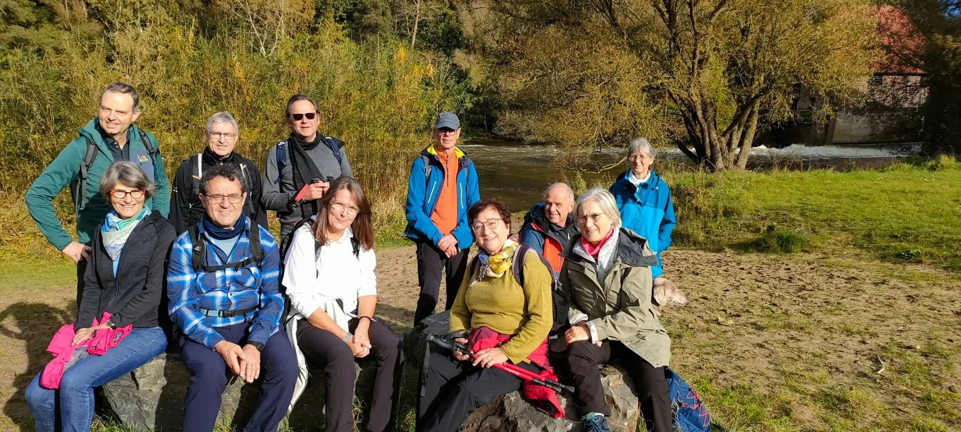 Gruppe von Wander*innen sitzt und steht entspannt auf Steinen an einem Flussufer bei sonnigem Wetter. | © DAV Dortmund