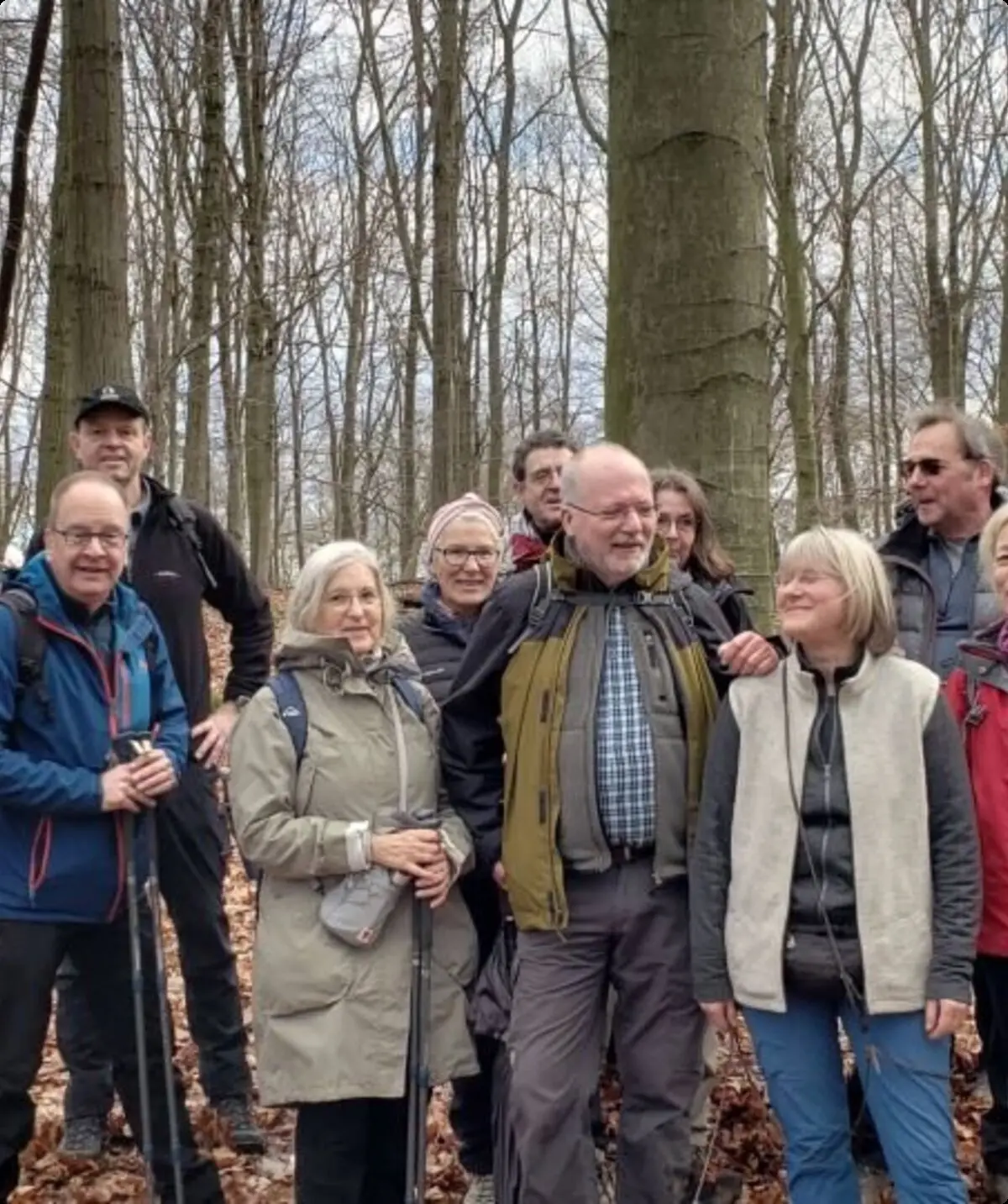 Ältere Wandergruppe steht lachend im Laubwald zwischen hohen Bäumen. | © DAV Dortmund