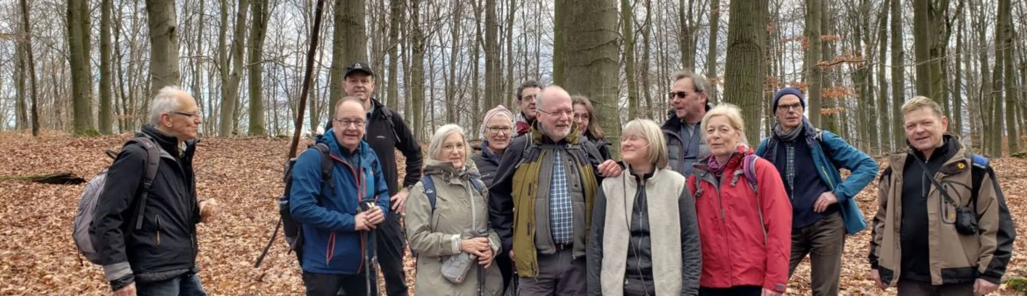 Ältere Wandergruppe steht lachend im Laubwald zwischen hohen Bäumen. | © DAV Dortmund