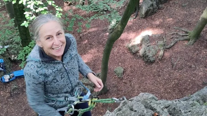 Eine Frau sichert sich beim Klettern an einem Felsen im Wald. | © DAV Dortmund