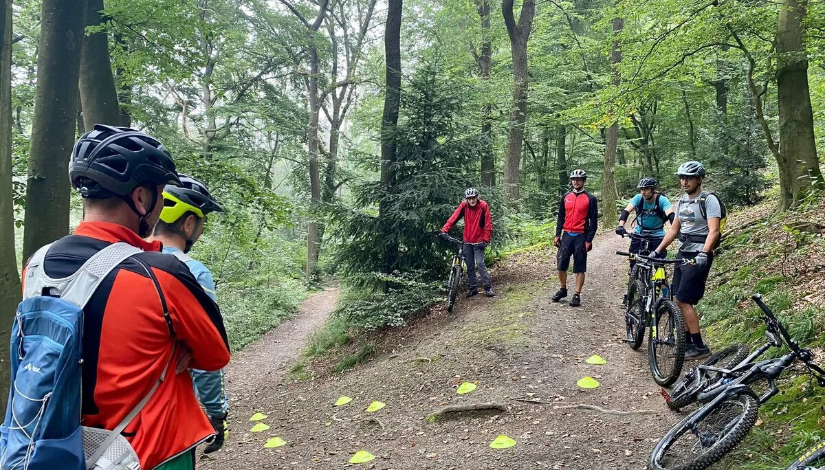 Mehrere Personen mit Mountainbikes bei einem Übungstraining auf einem Waldweg mit Markierungshütchen. | © DAV Dortmund