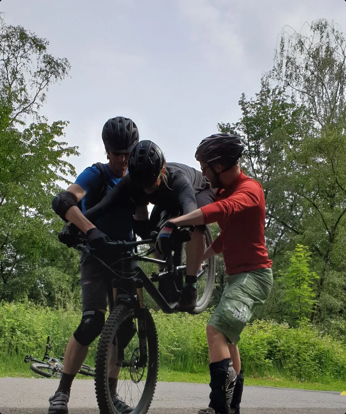 Drei Mountainbiker*innen stehen zusammen, einer auf dem Rad – technische Übungssituation. | © DAV Dortmund