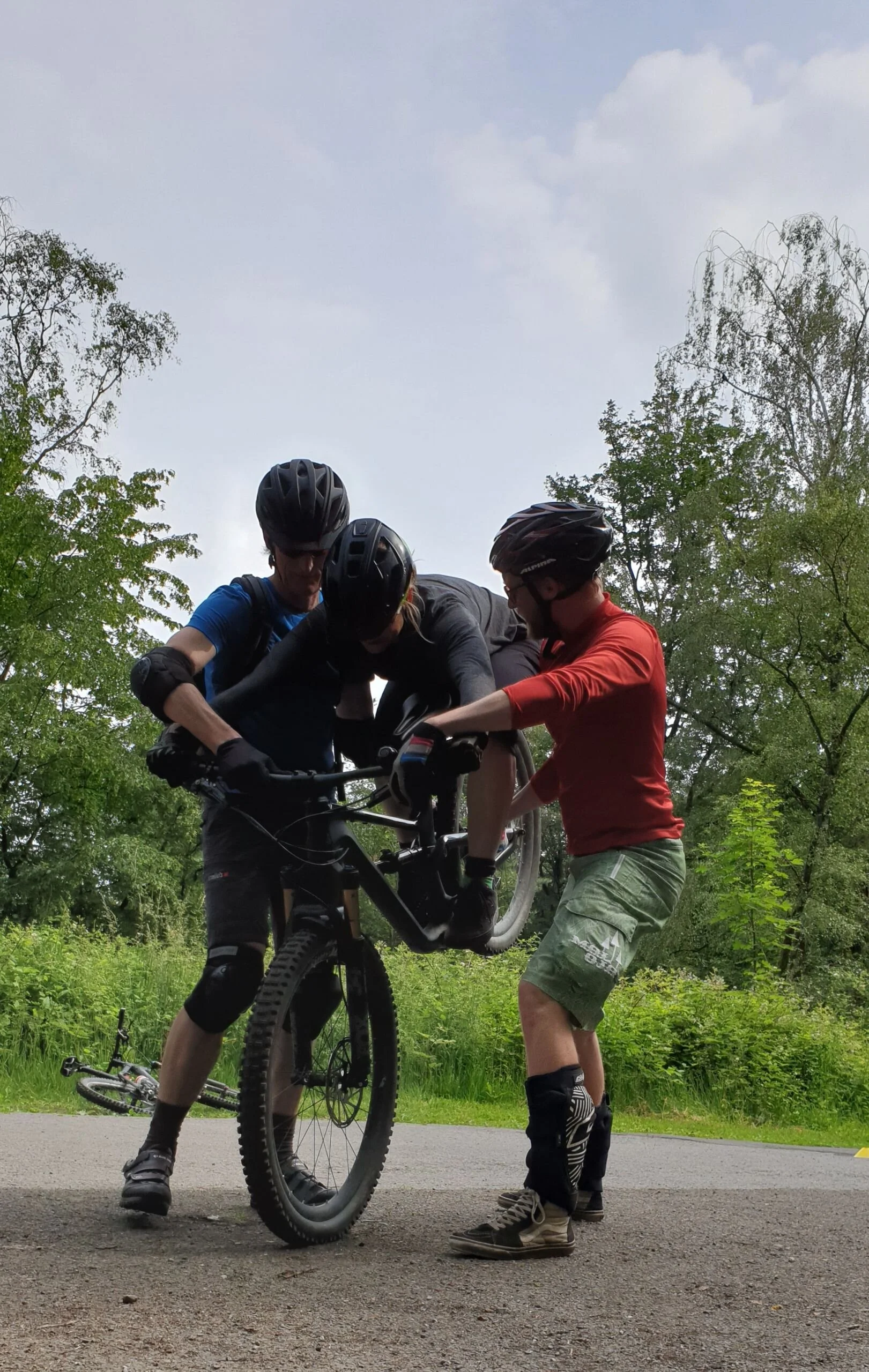 Drei Mountainbiker*innen stehen zusammen, einer auf dem Rad – technische Übungssituation. | © DAV Dortmund