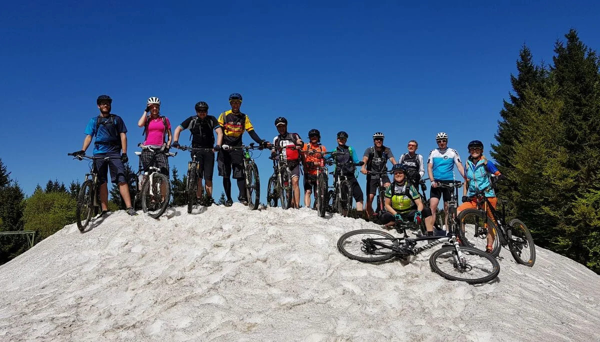 Gruppe von Mountainbiker*innen posiert auf einem verschneiten Hügel mit blauem Himmel. | © DAV Dortmund
