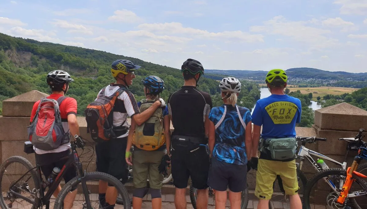 Mountainbike-Gruppe steht an einer Mauer mit Blick ins grüne Tal. | © DAV Dortmund