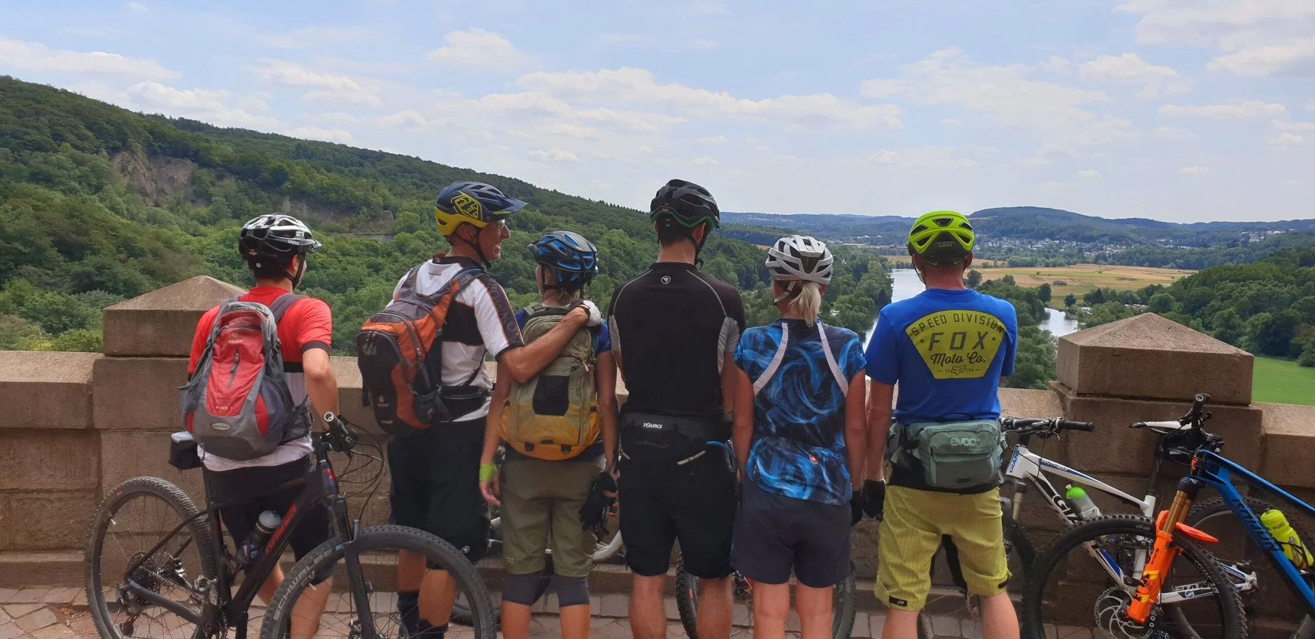 Mountainbike-Gruppe steht an einer Mauer mit Blick ins grüne Tal. | © DAV Dortmund