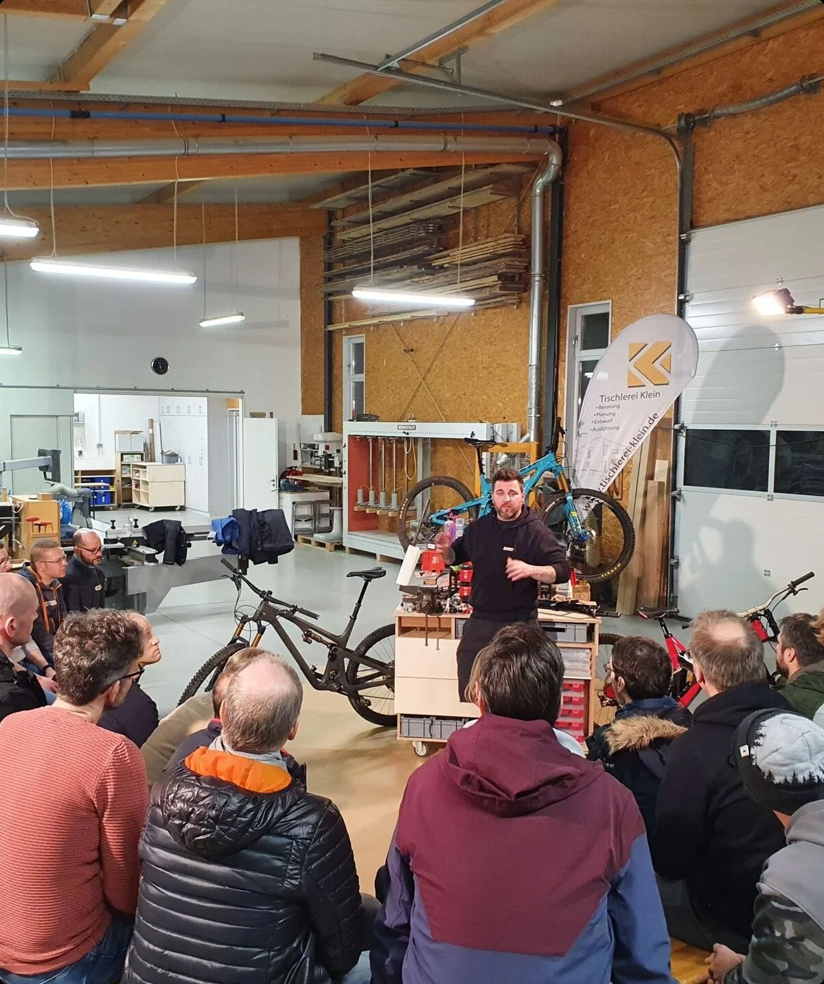 Gruppe von Personen in einer Werkstatt hört einem Vortrag über Fahrräder zu, im Hintergrund Werkzeuge und Werkbänke. | © DAV Dortmund
