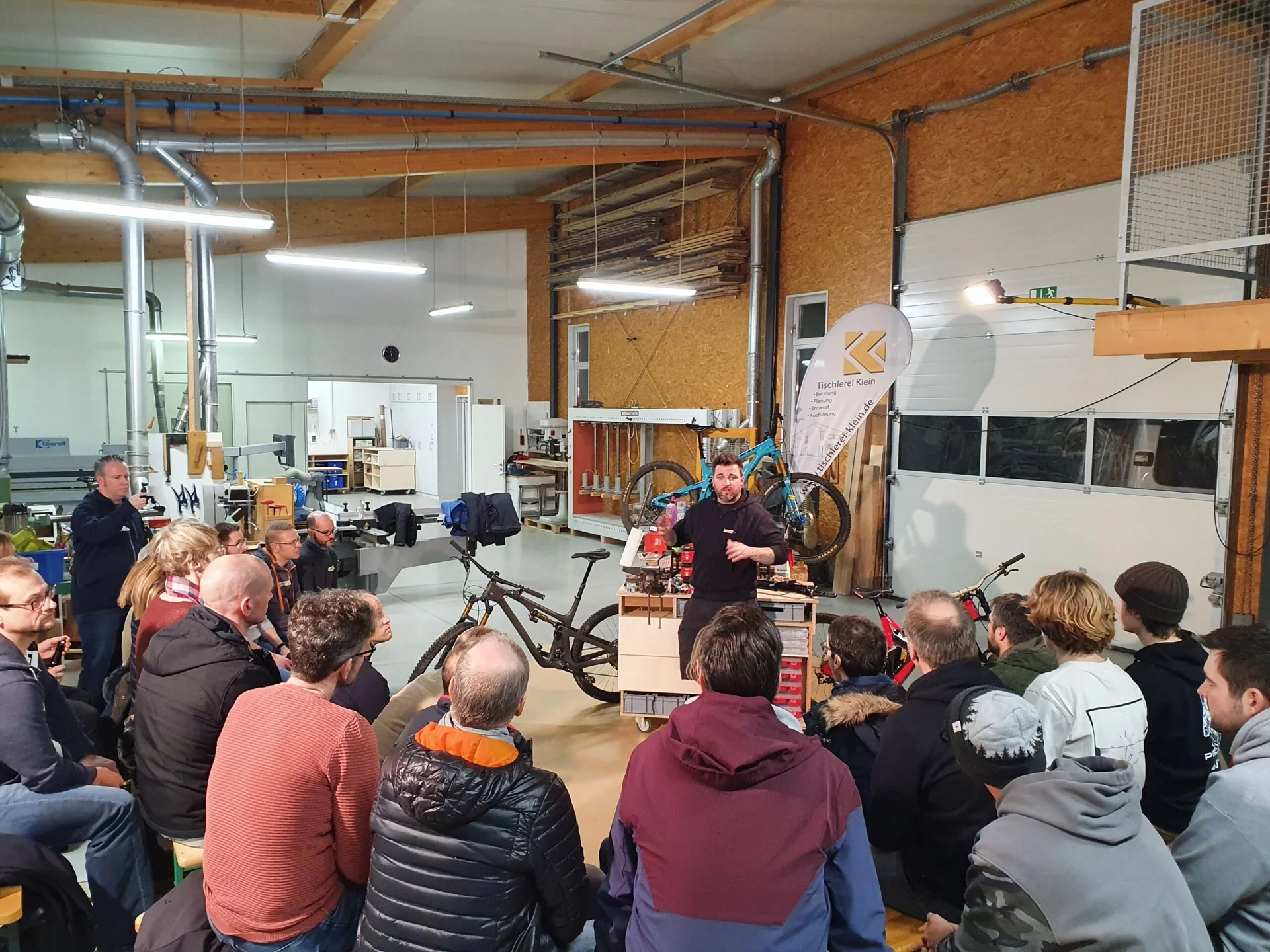 Gruppe von Personen in einer Werkstatt hört einem Vortrag über Fahrräder zu, im Hintergrund Werkzeuge und Werkbänke. | © DAV Dortmund