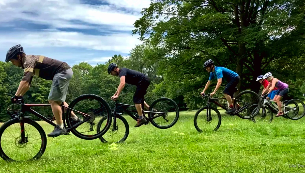 Vier Personen üben gleichzeitig eine Mountainbike-Technik auf einer Wiese mit Bäumen im Hintergrund. | © DAV Dortmund