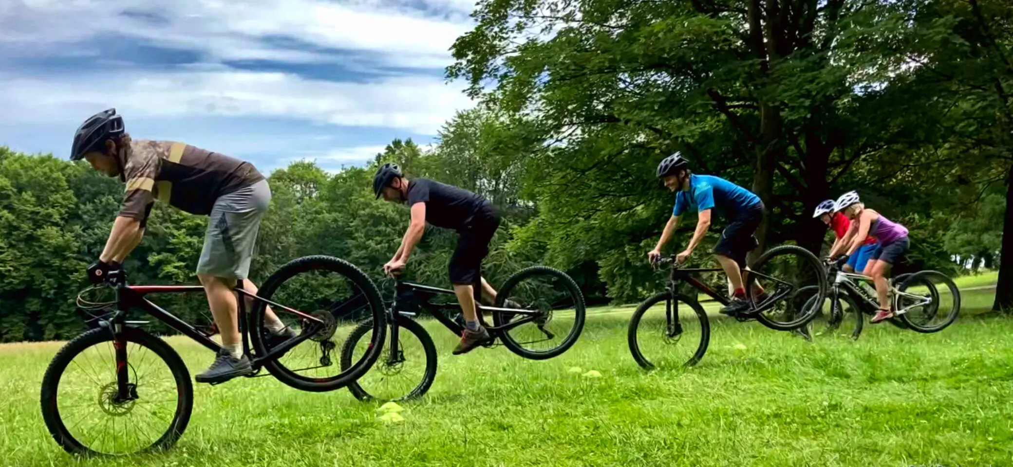 Vier Personen üben gleichzeitig eine Mountainbike-Technik auf einer Wiese mit Bäumen im Hintergrund. | © DAV Dortmund