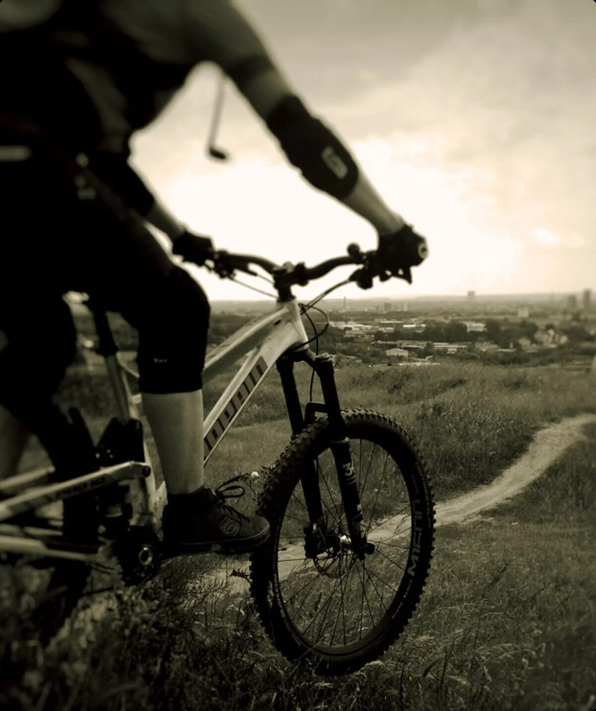 Eine Person fährt mit dem Mountainbike einen schmalen Pfad entlang, im Hintergrund eine Stadtlandschaft. | © DAV Dortmund