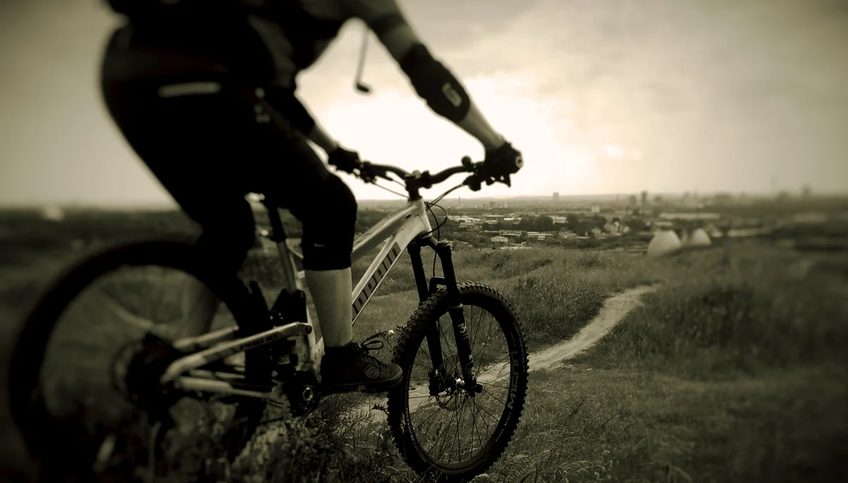 Eine Person fährt mit dem Mountainbike einen schmalen Pfad entlang, im Hintergrund eine Stadtlandschaft. | © DAV Dortmund