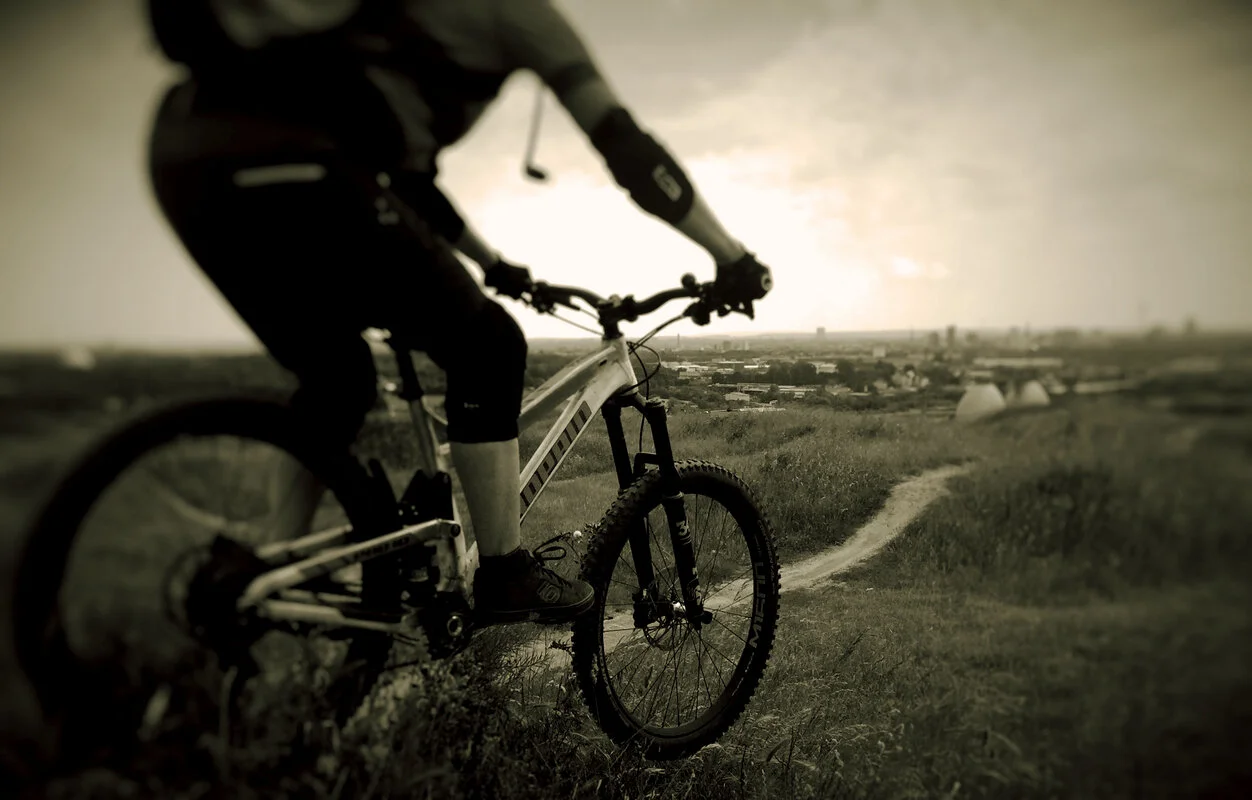 Eine Person fährt mit dem Mountainbike einen schmalen Pfad entlang, im Hintergrund eine Stadtlandschaft. | © DAV Dortmund