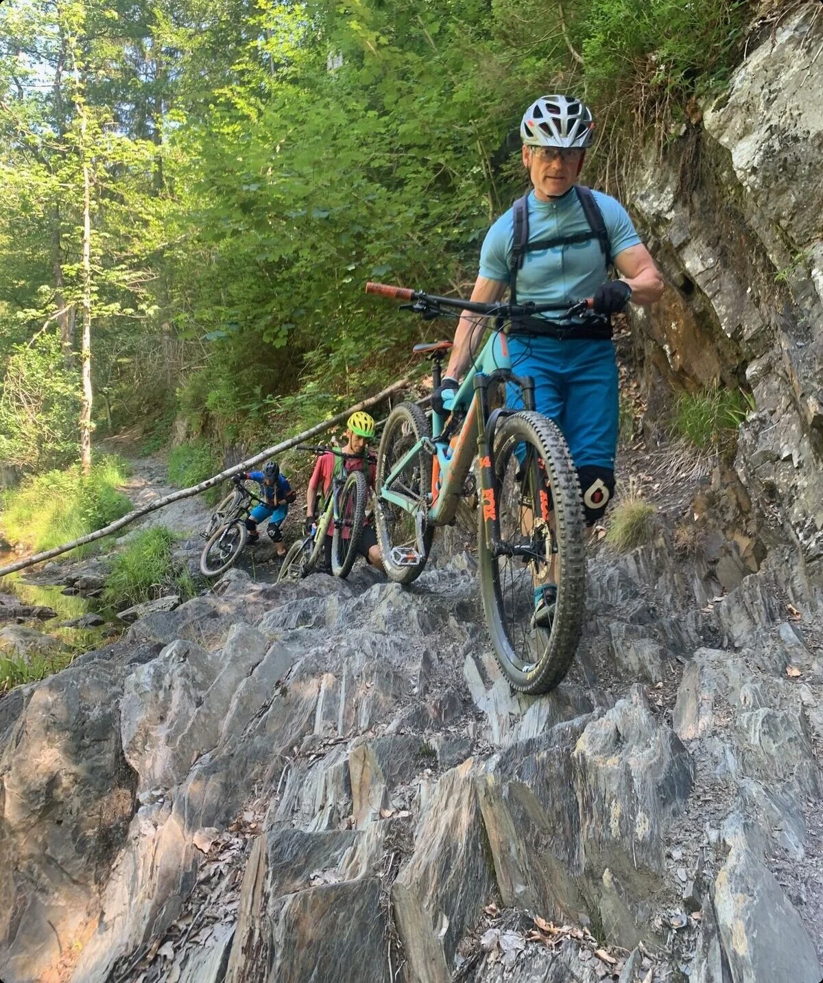 Mountainbiker*innen schieben ihre Räder über einen schmalen, felsigen Pfad im Wald. | © DAV Dortmund