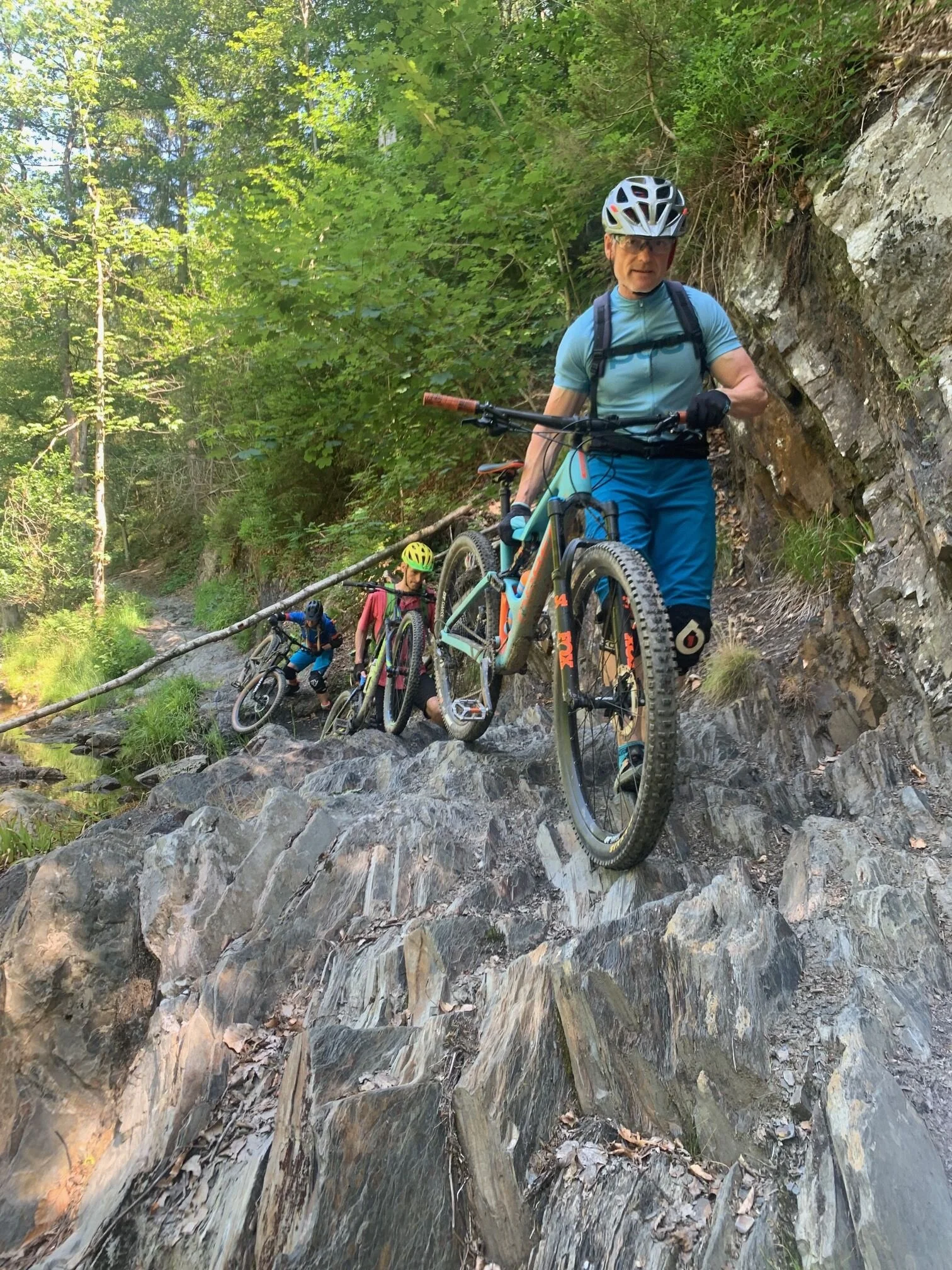 Mountainbiker*innen schieben ihre Räder über einen schmalen, felsigen Pfad im Wald. | © DAV Dortmund