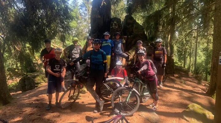 Mountainbike-Gruppe steht im Schatten großer Bäume bei einem Felsen im Wald. | © DAV Dortmund