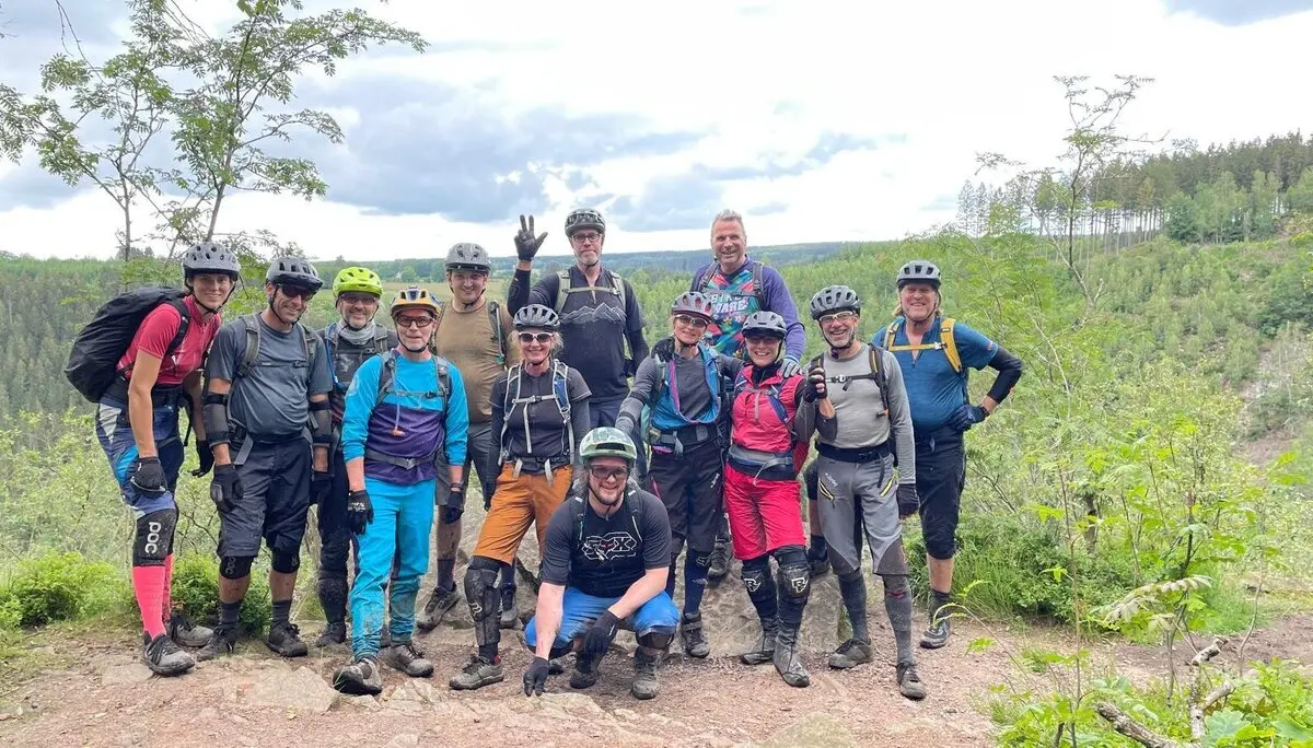 Eine große Gruppe von Mountainbiker*innen posiert gemeinsam auf einem Felsen mit Ausblick. | © DAV Dortmund