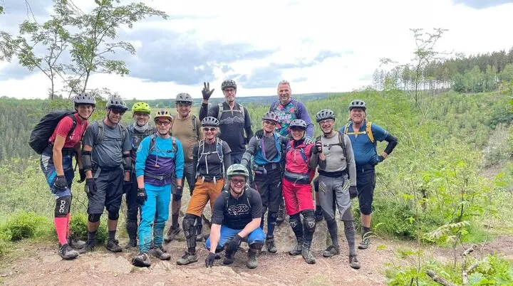 Eine große Gruppe von Mountainbiker*innen posiert gemeinsam auf einem Felsen mit Ausblick. | © DAV Dortmund