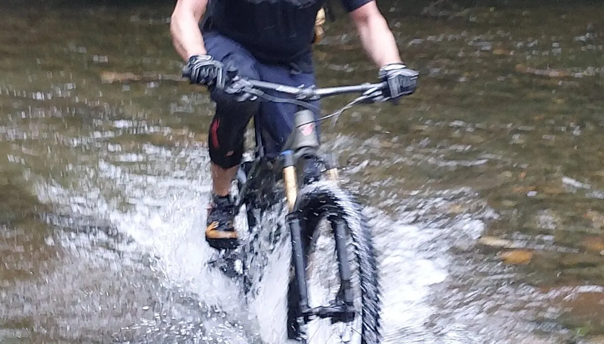 Ein Mountainbiker durchquert einen flachen Fluss auf einem schmalen Pfad im Wald. | © DAV Dortmund 