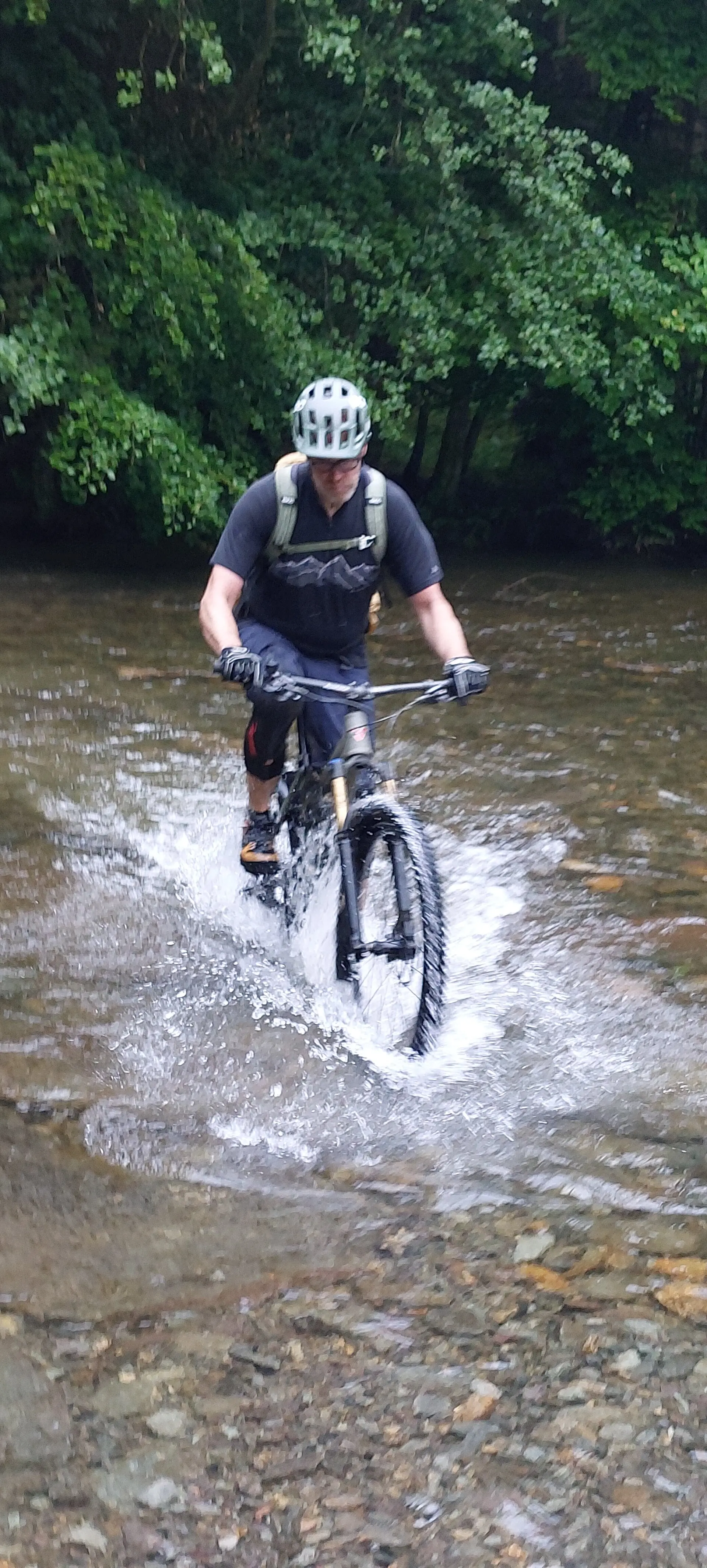 Ein Mountainbiker durchquert einen flachen Fluss auf einem schmalen Pfad im Wald. | © DAV Dortmund 