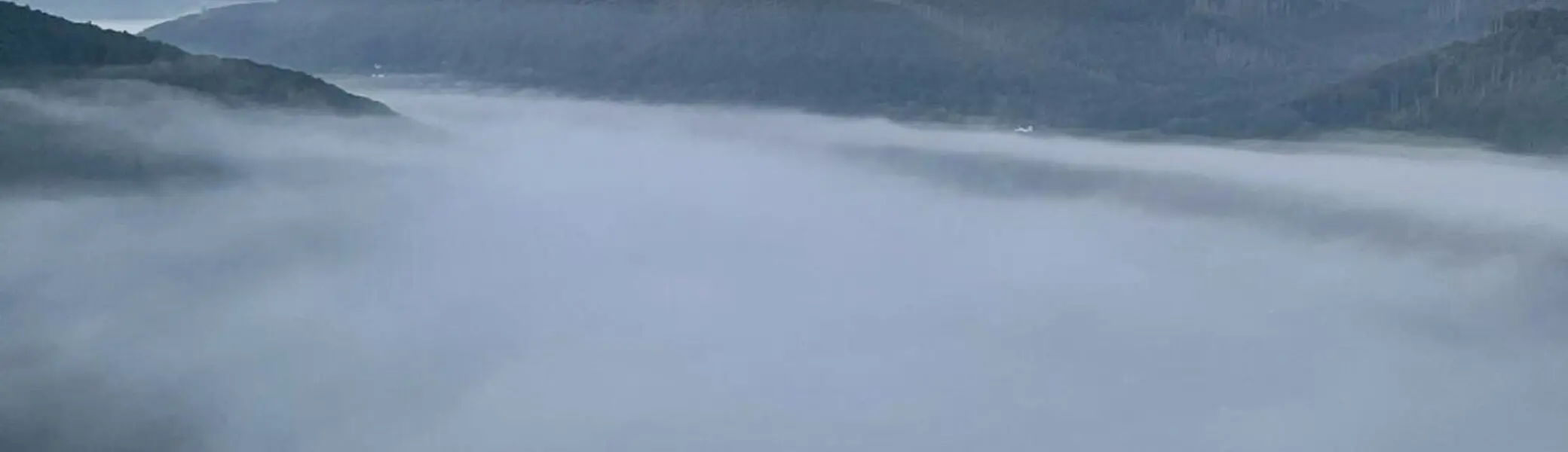 Dichte Nebelschwaden füllen ein Tal zwischen bewaldeten Hügeln unter einem klaren Morgenhimmel. | © DAV Dortmund