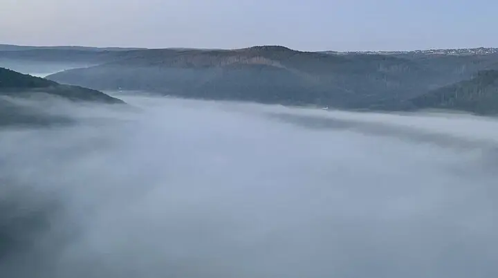 Dichte Nebelschwaden füllen ein Tal zwischen bewaldeten Hügeln unter einem klaren Morgenhimmel. | © DAV Dortmund