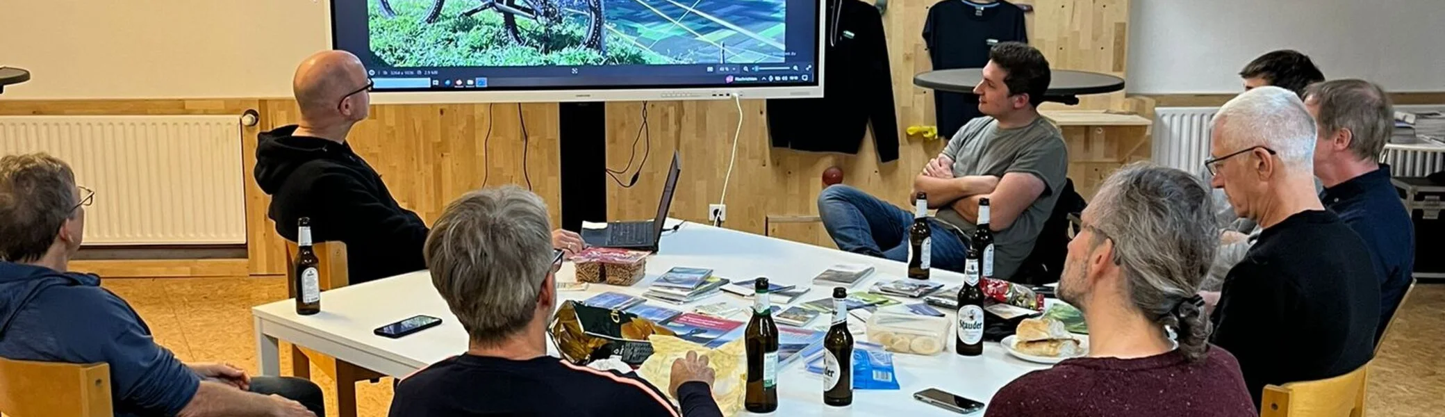 Gruppe von Personen schaut sich eine Mountainbike-Präsentation auf einem großen Bildschirm an. | © dav mtb