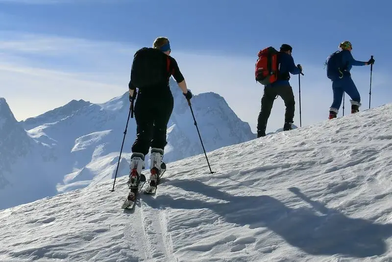 Drei Skitourengeher*innen steigen mit Tourenski bei gutem Wetter durch die verschneite Berglandschaft. | © DAV Dortmund
