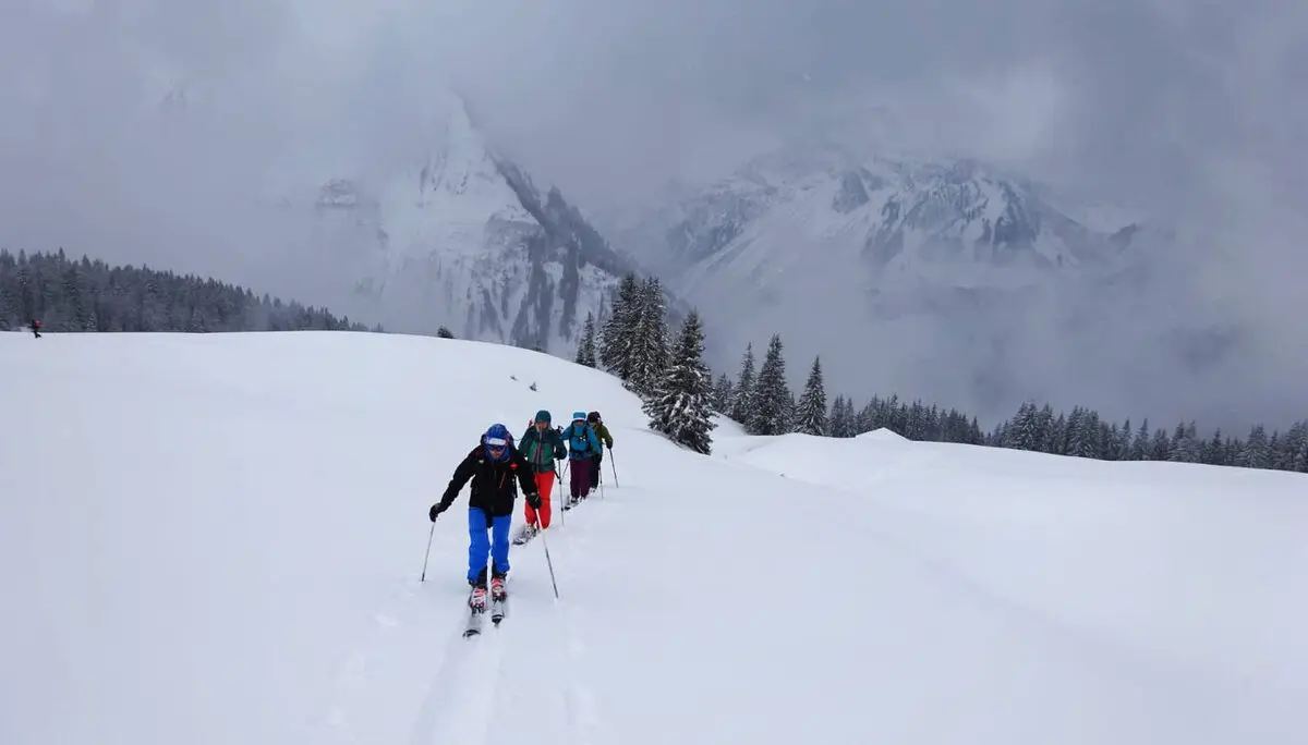 Skitourengruppe geht in einer Reihe durch tiefen Neuschnee, im Hintergrund verschneite Berge. | © DAV Dortmund