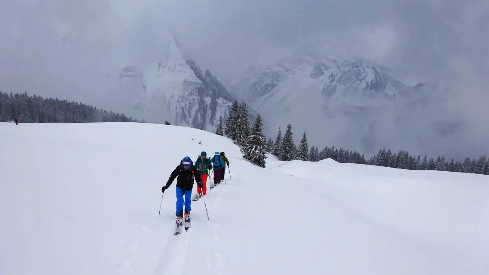 Skitourengruppe geht in einer Reihe durch tiefen Neuschnee, im Hintergrund verschneite Berge. | © DAV Dortmund