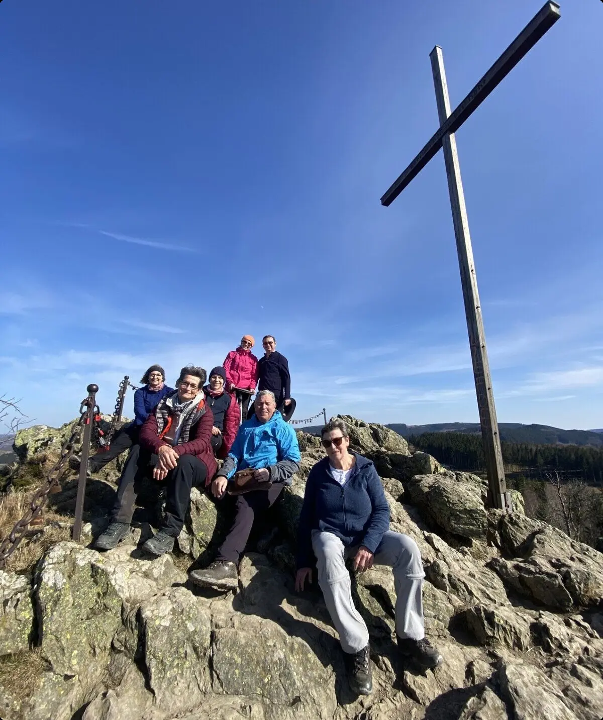 Wandergruppe sitzt entspannt neben einem großen Holzkreuz auf einem felsigen Gipfel. | © DAV Dortmund