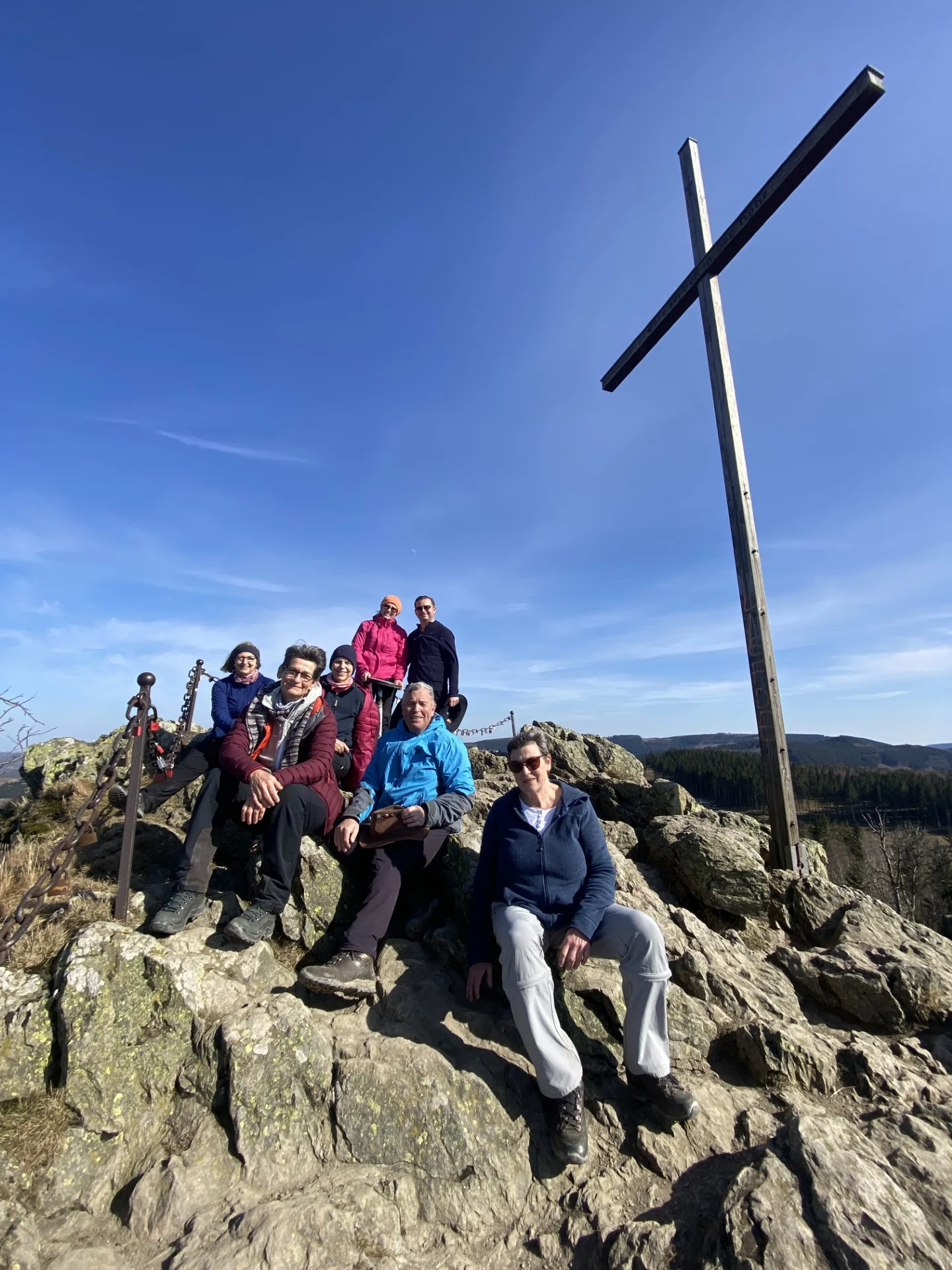 Wandergruppe sitzt entspannt neben einem großen Holzkreuz auf einem felsigen Gipfel. | © DAV Dortmund