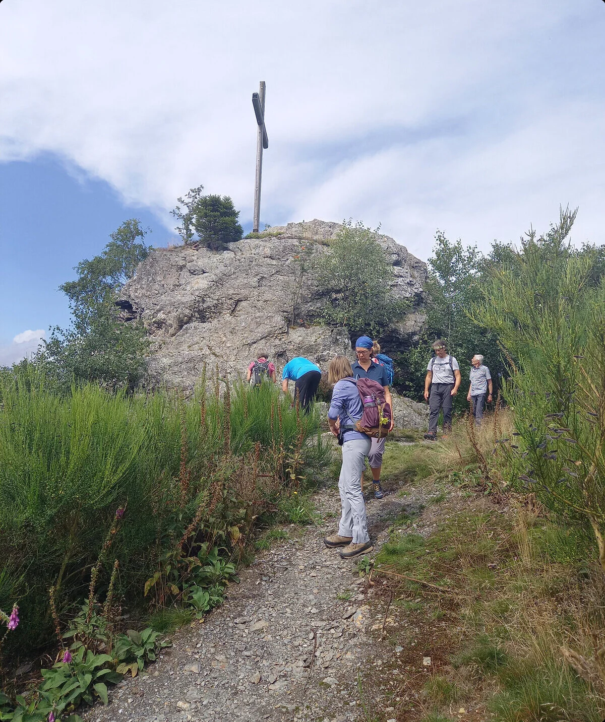 Mehrere Personen wandern auf einem schmalen Pfad zu einem Felsen mit Gipfelkreuz. | © DAV Dortmund