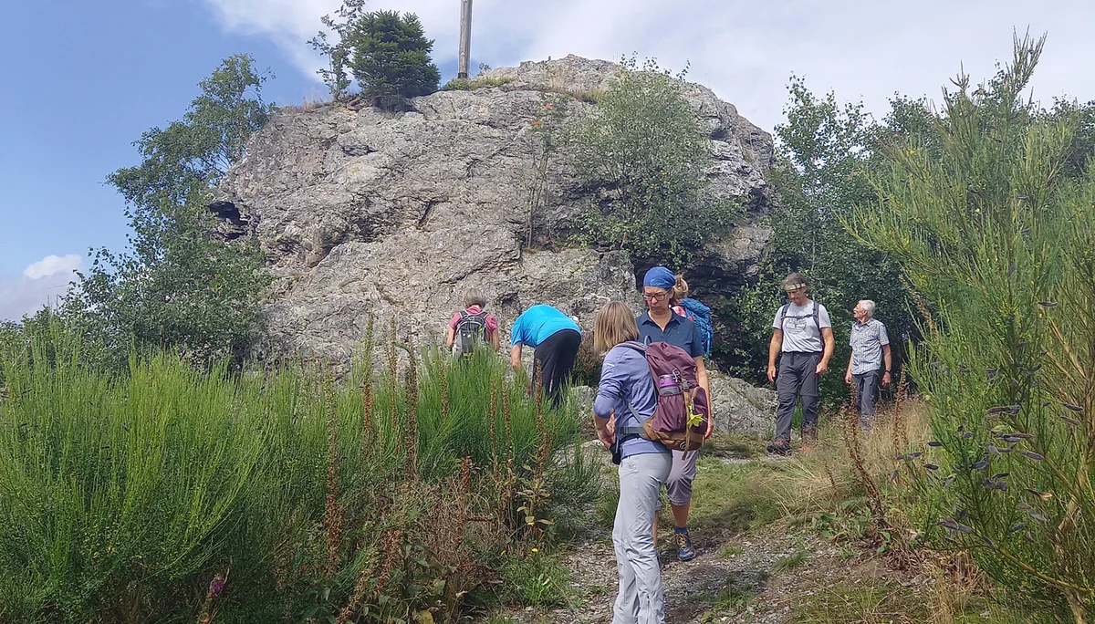 Mehrere Personen wandern auf einem schmalen Pfad zu einem Felsen mit Gipfelkreuz. | © DAV Dortmund