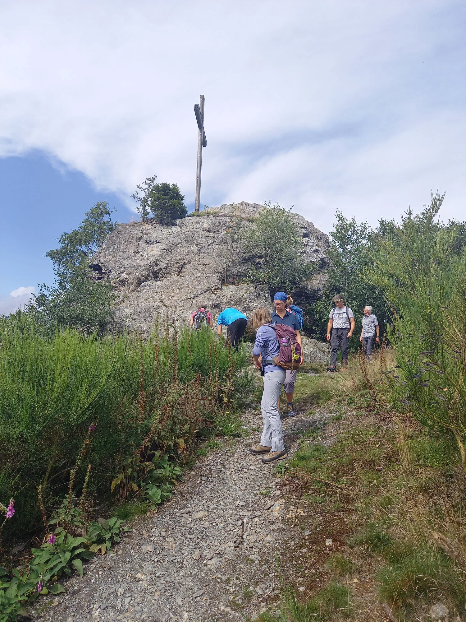 Mehrere Personen wandern auf einem schmalen Pfad zu einem Felsen mit Gipfelkreuz. | © DAV Dortmund