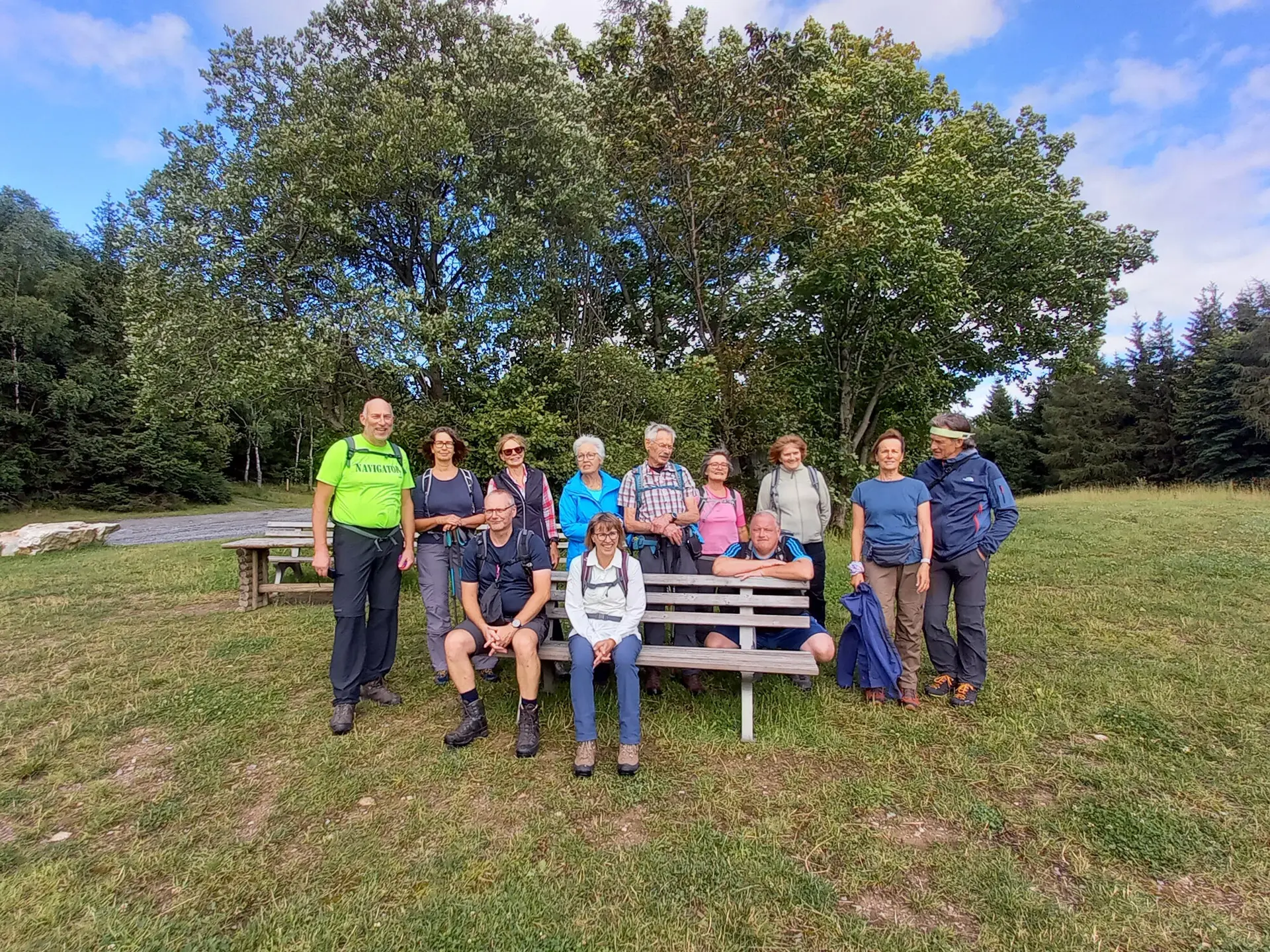 Eine Gruppe von Wandernden posiert auf einer Wiese neben Bänken unter Bäumen. | © DAV Dortmund