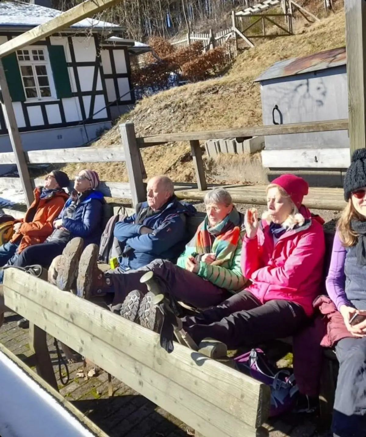 Gruppe von Wander*innen sitzt auf Holzbänken vor einem Fachwerkhaus und genießt die Sonne im Winter. | © DAV Dortmund