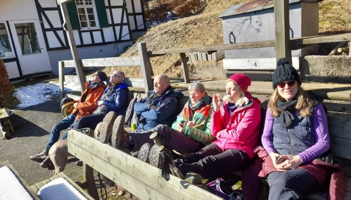 Gruppe von Wander*innen sitzt auf Holzbänken vor einem Fachwerkhaus und genießt die Sonne im Winter. | © DAV Dortmund