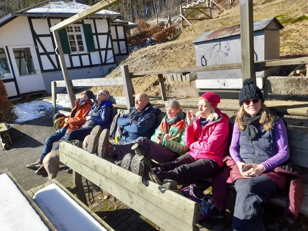 Gruppe von Wander*innen sitzt auf Holzbänken vor einem Fachwerkhaus und genießt die Sonne im Winter. | © DAV Dortmund