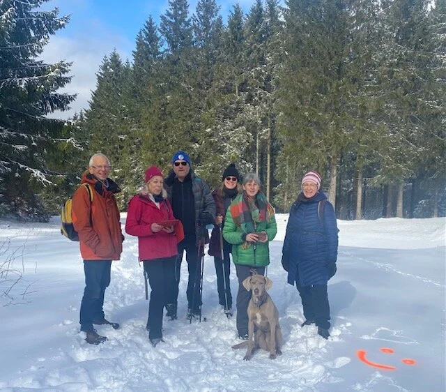 Sieben Personen und ein Hund stehen im Schnee auf einem Weg im Wald, im Vordergrund ein Smiley im Schnee. | © DAV Dortmund
