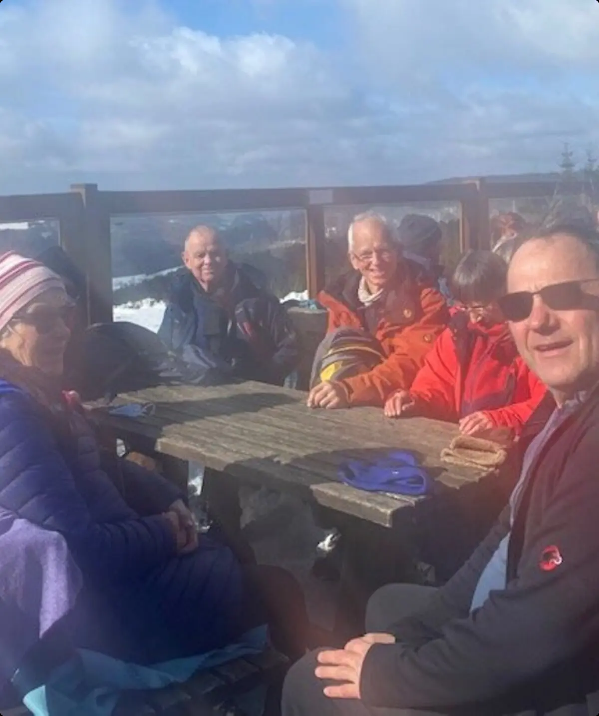 Wandergruppe sitzt bei sonnigem Wetter auf Holzbänken einer Terrasse im Schnee. | © DAV Dortmund