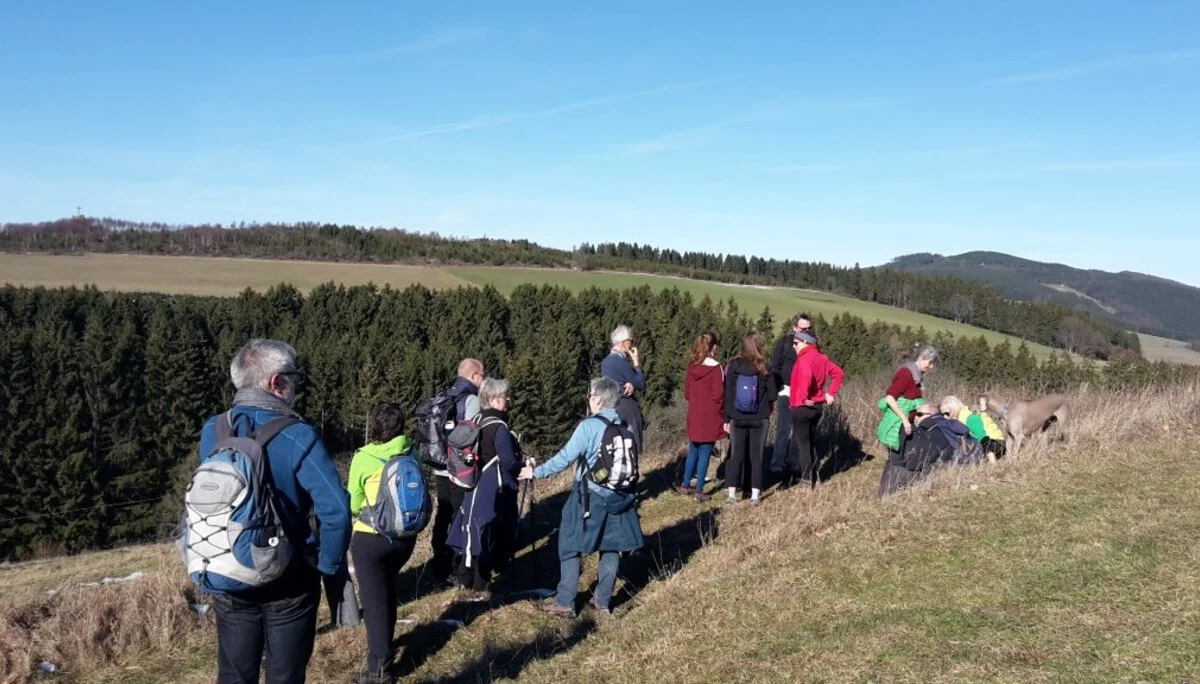 Wandergruppe steht auf einer Anhöhe mit Blick auf Wald und Felder unter blauem Himmel. | © DAV Dortmund