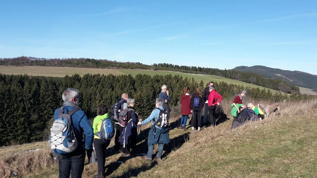 Wandergruppe steht auf einer Anhöhe mit Blick auf Wald und Felder unter blauem Himmel. | © DAV Dortmund
