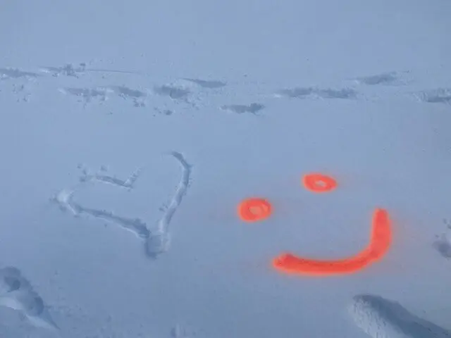 Ein Herz wurde in den Schnee gezeichnet, daneben ein orangefarbenes Smiley aus Sprühfarbe. | © DAV Dortmund